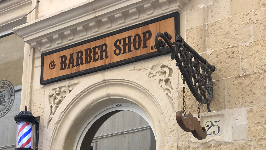 L'insegna in legno del Barbershop GF sulla facciata in pietra leccese